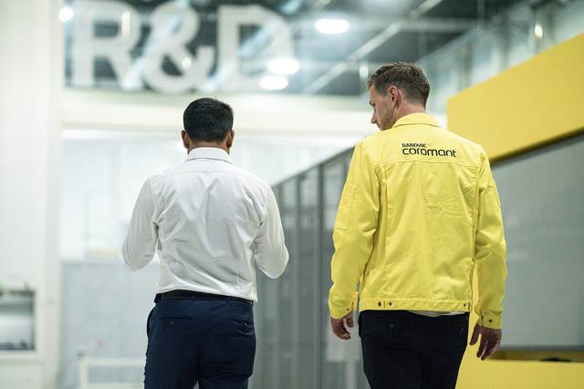 Two professionals walking through a spacious, modern Sandvik Coromant facility toward a large R&D si