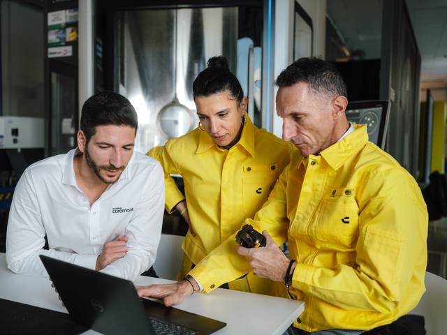 Three Sandvik Coromant team members collaborating around a laptop, with two experts in yellow workwe